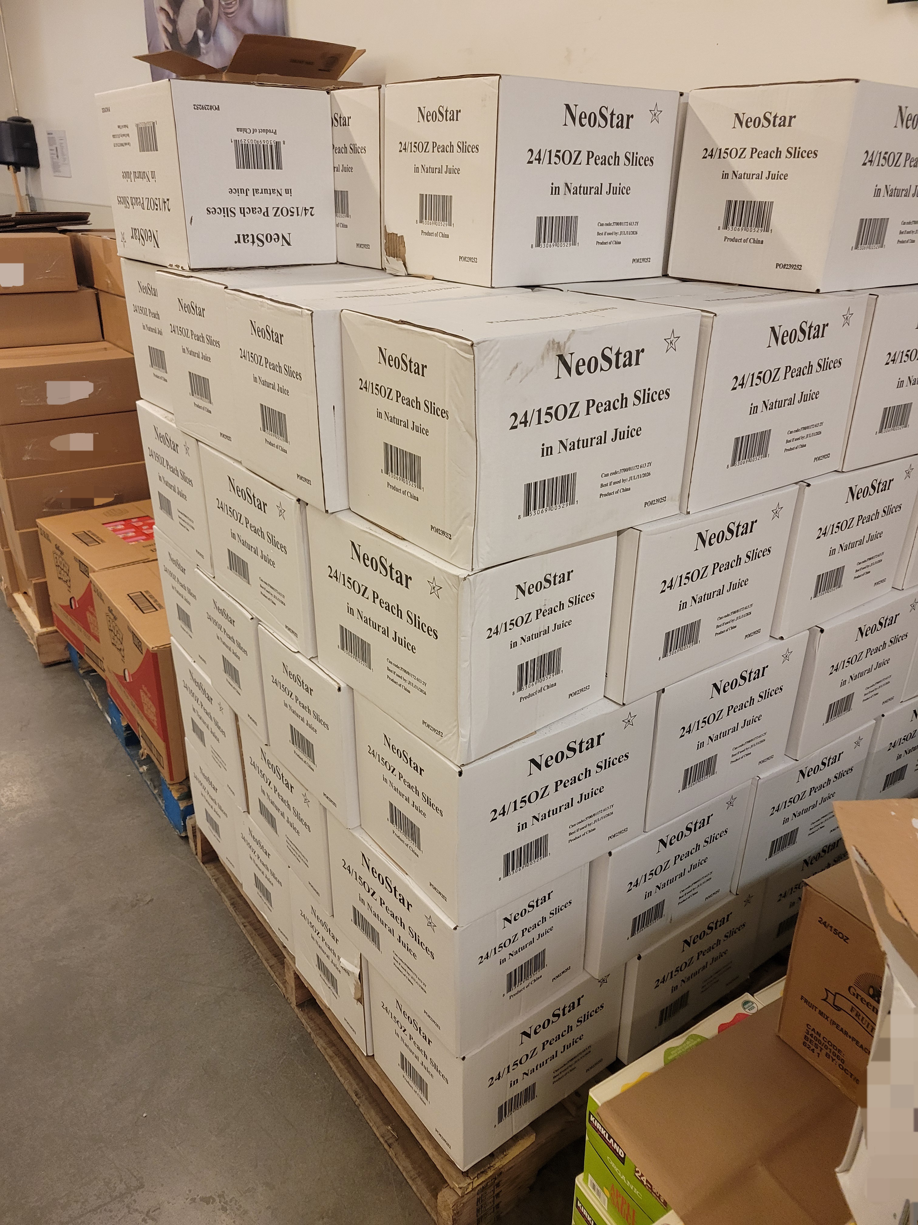 Different food products on wooden pallets with boxes of canned peach slices in the center.